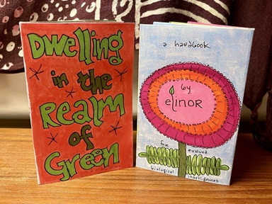 a brightly colored zine on a teakwood desk with a burgundy tapestry in the background